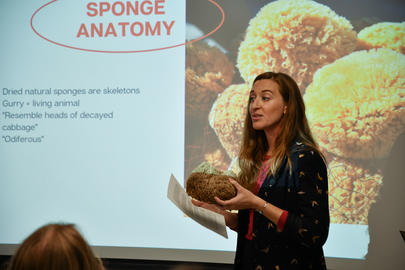 A presenter hold a marine sponge while standing in front of a projector screen.