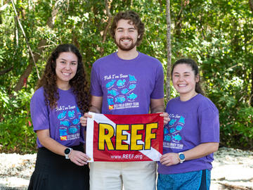 Three Spring 2023 Marine Conservation Interns holding a REEF flag.